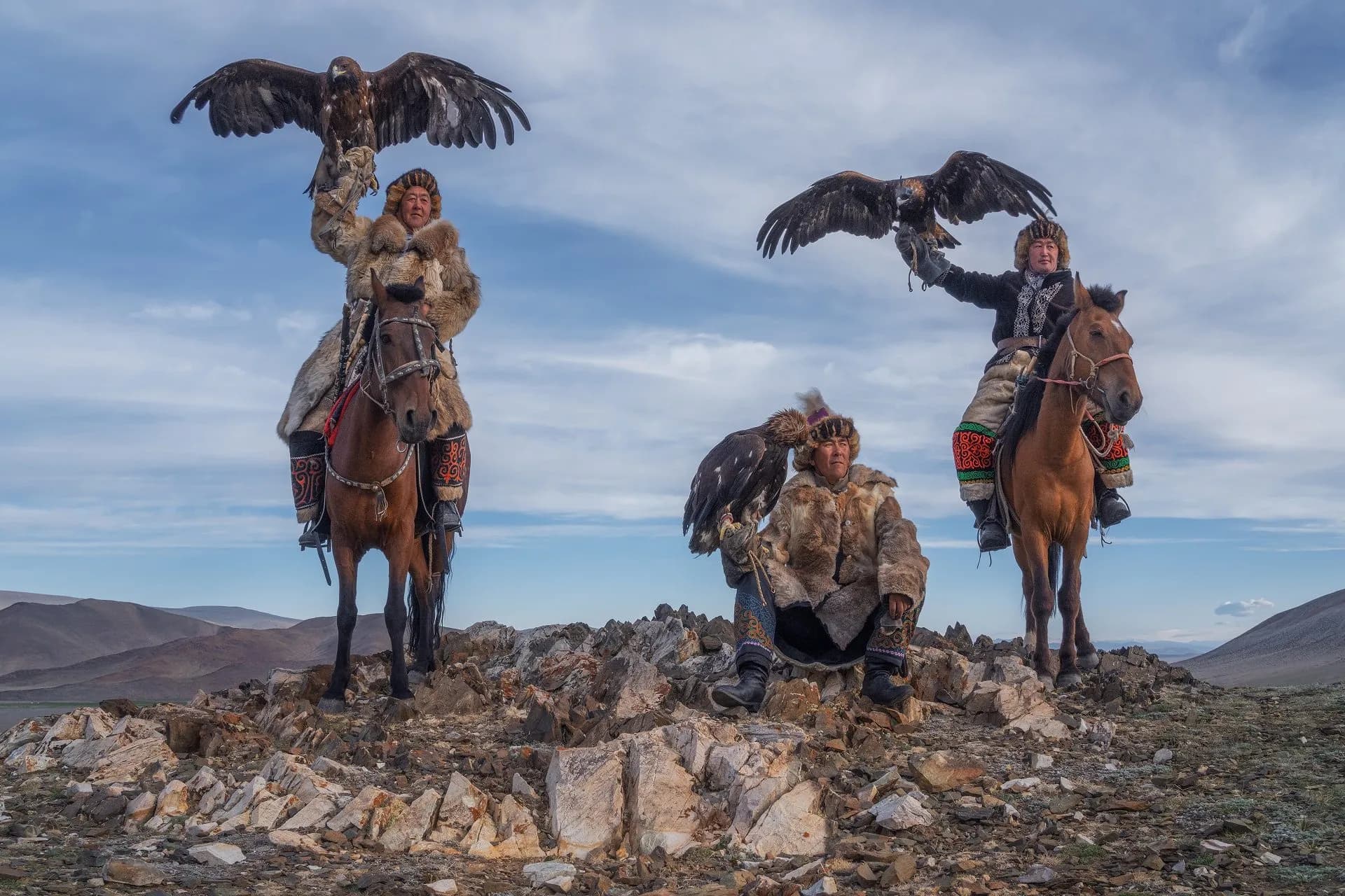 Kazakh eagle hunters with golden eagles on a mountain ridge
